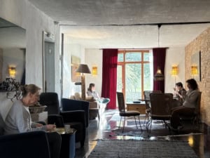 Cozy hotel lounge with customers seated on armchairs, warm lamps, and a red-curtain window at the far end