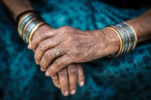 Close-up of an elderly hand with turquoise and gold bangles and a floral ring on the index finger.