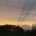 Sunset scene with orange glow over a dark treeline and cloudy sky in the distance.