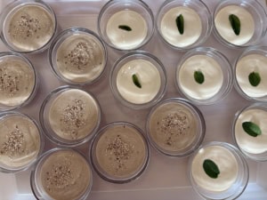 Assorted dessert cups: beige pudding topped with sesame seeds and white custard cups with a mint leaf garnish.