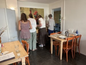 Group of people serving themselves at a long dining table in a bright kitchen area, viewed from behind.